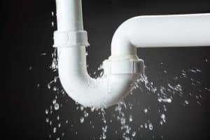A close-up photo of a broken white pipe spraying water in a house. Burst water pipe in house.